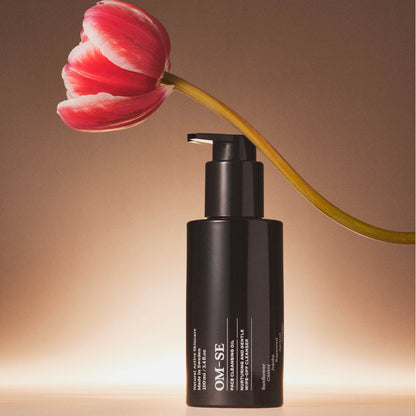 OM-SE Face Cleansing Oil bottle with pump dispenser next to a red tulip on a warm brown background